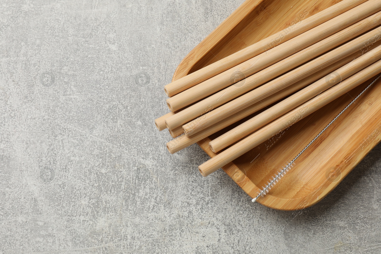 Photo of Bamboo drinking straws and cleaning brush on grey textured table, top view. Space for text