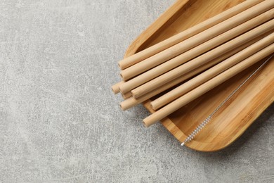 Photo of Bamboo drinking straws and cleaning brush on grey textured table, top view. Space for text