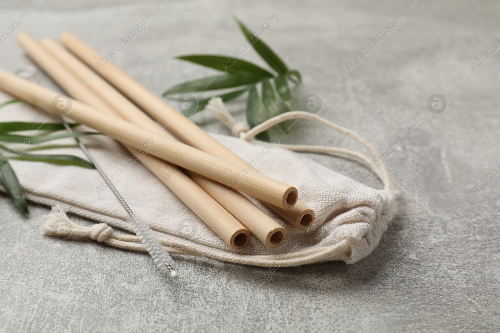 Photo of Bamboo drinking straws, cleaning brush and bag on grey textured table, closeup