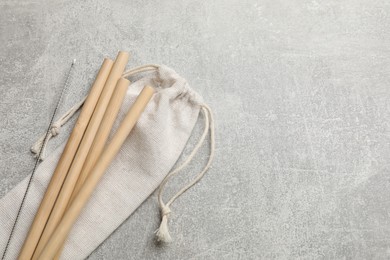 Photo of Bamboo drinking straws, cleaning brush and bag on grey textured table, top view. Space for text