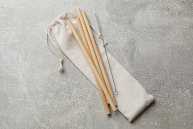 Photo of Bamboo drinking straws, cleaning brush and bag on grey textured table, top view