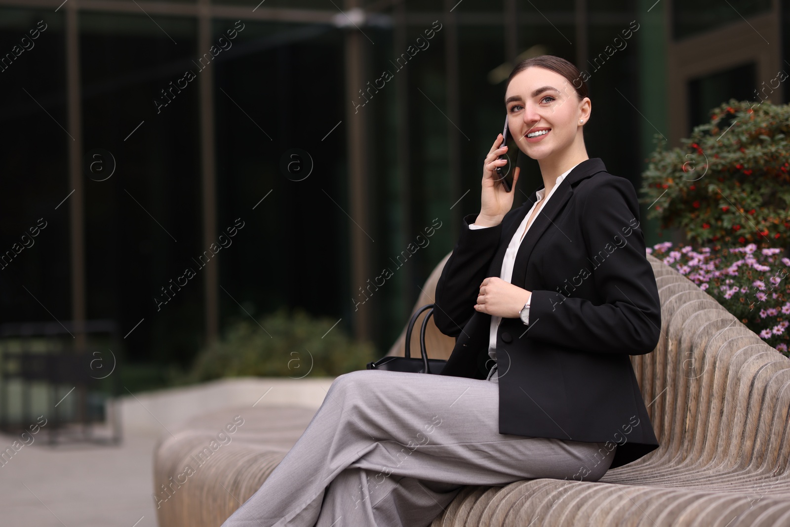 Photo of Woman in stylish formal suit talking on phone outdoors. Space for text