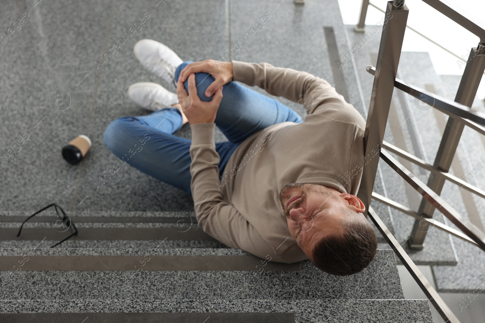 Photo of Man with injured knee on stairs in building after fall, above view. Dangerous accident