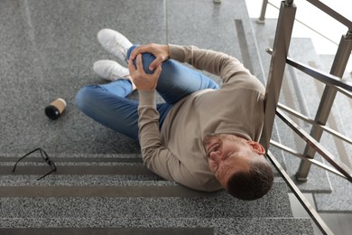 Man with injured knee on stairs in building after fall, above view. Dangerous accident