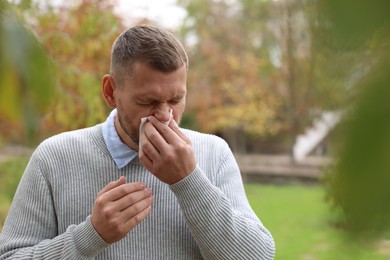 Man with tissue blowing runny nose in park