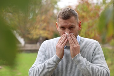 Photo of Man with tissue blowing runny nose in park