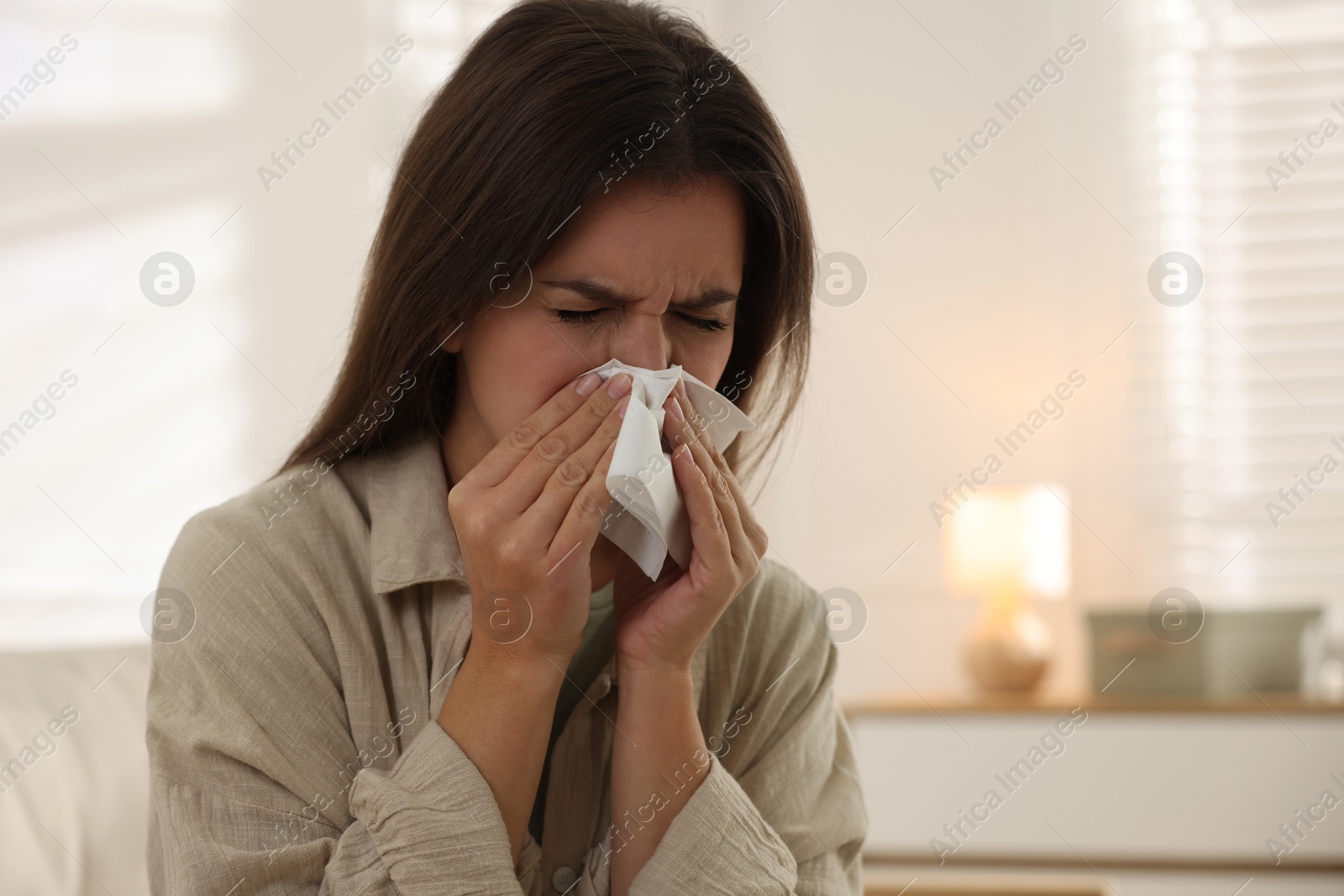 Photo of Young woman with tissue blowing runny nose at home