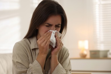 Young woman with tissue blowing runny nose at home