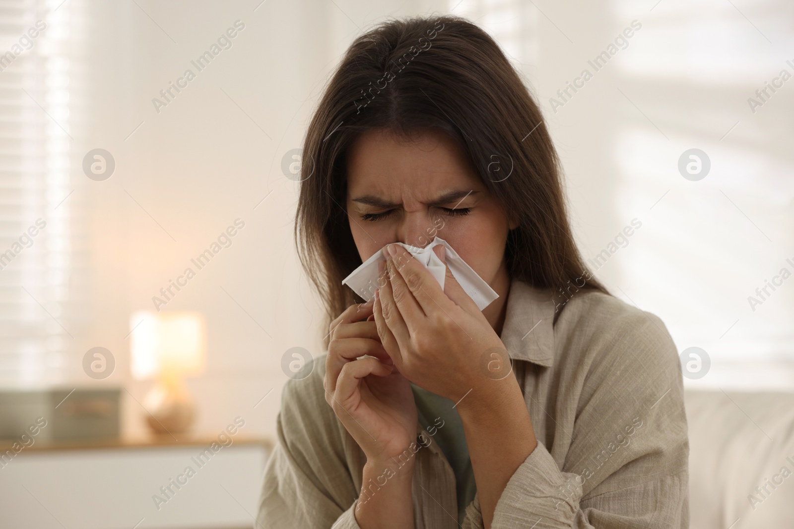 Photo of Young woman with tissue blowing runny nose at home