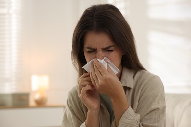 Young woman with tissue blowing runny nose at home