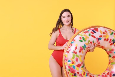 Photo of Beautiful woman in swimsuit with inflatable ring on yellow background. Space for text