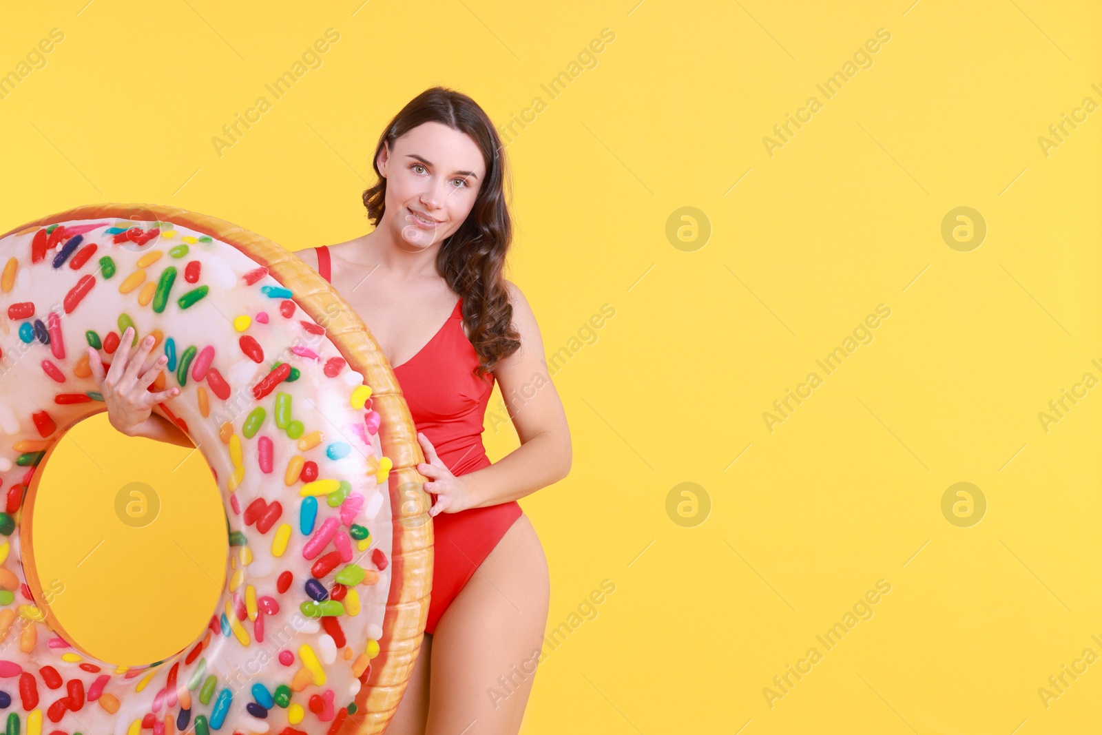 Photo of Beautiful woman in swimsuit with inflatable ring on yellow background. Space for text