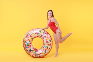 Photo of Beautiful woman in swimsuit with inflatable ring on yellow background