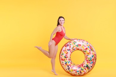 Photo of Beautiful woman in swimsuit with inflatable ring on yellow background