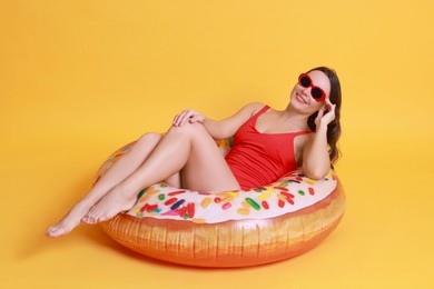 Photo of Beautiful woman in swimsuit with inflatable ring on yellow background