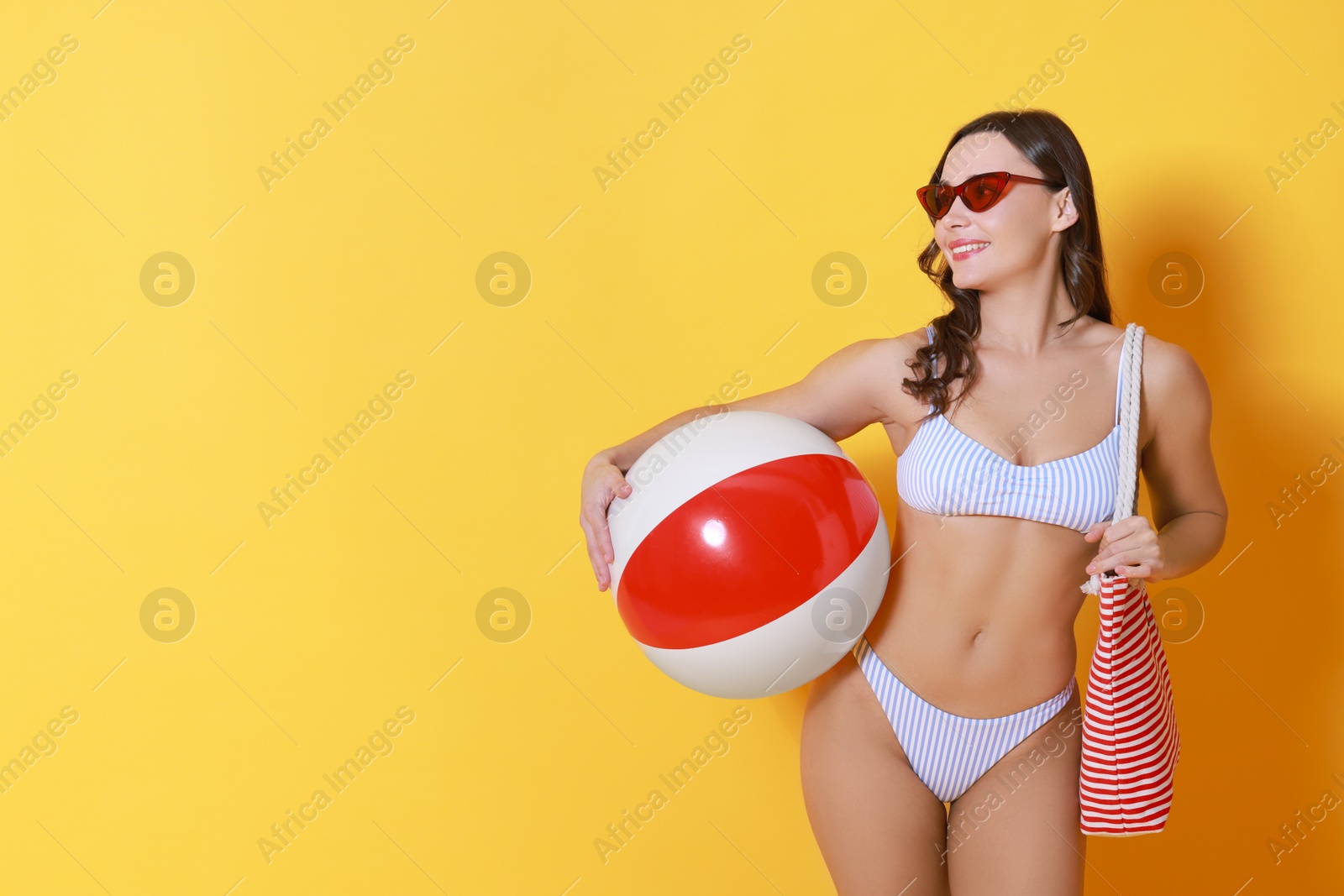 Photo of Beautiful woman in swimsuit with inflatable ball on yellow background. Space for text