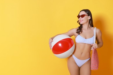 Beautiful woman in swimsuit with inflatable ball on yellow background. Space for text