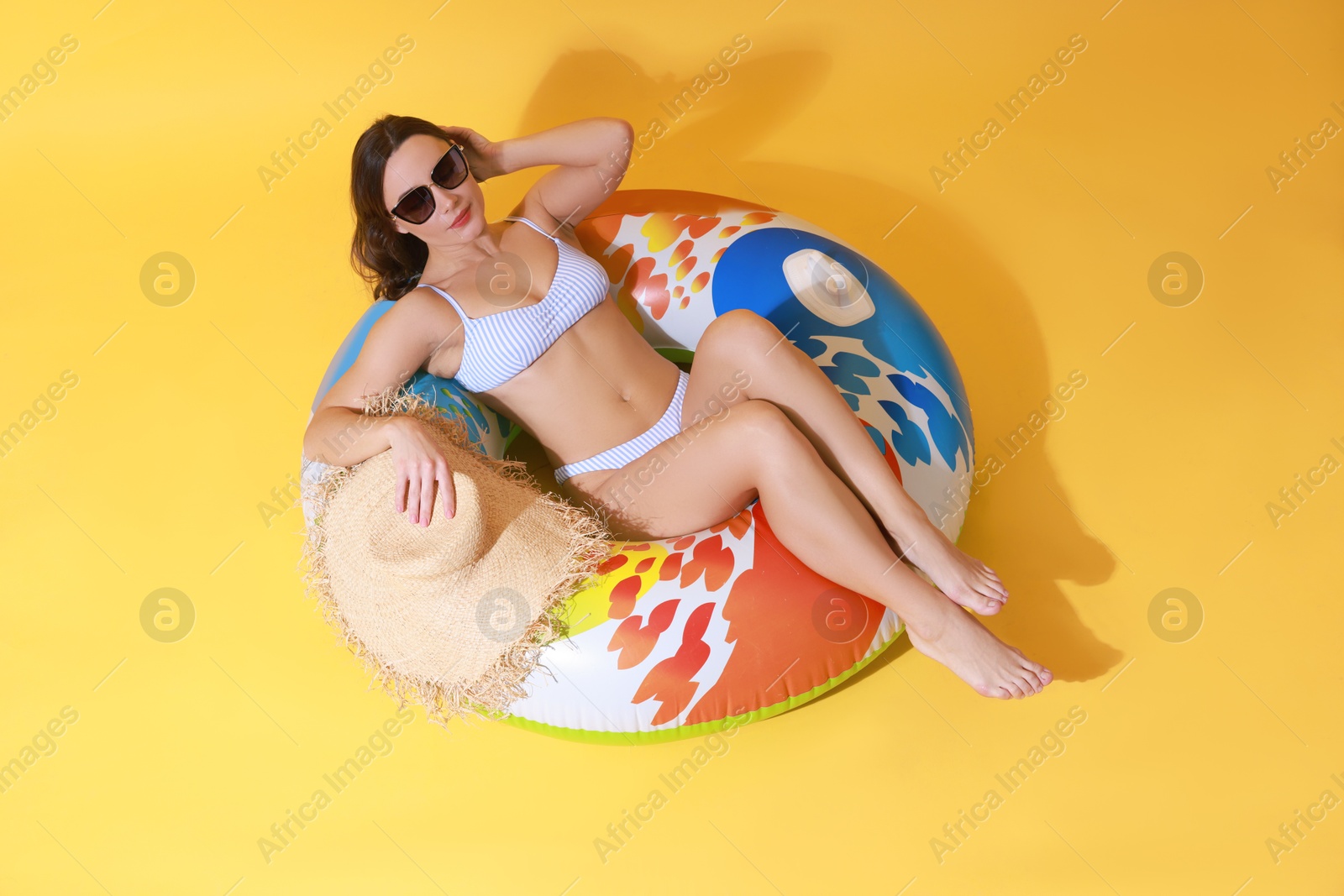 Photo of Beautiful woman in swimsuit with inflatable ring on yellow background