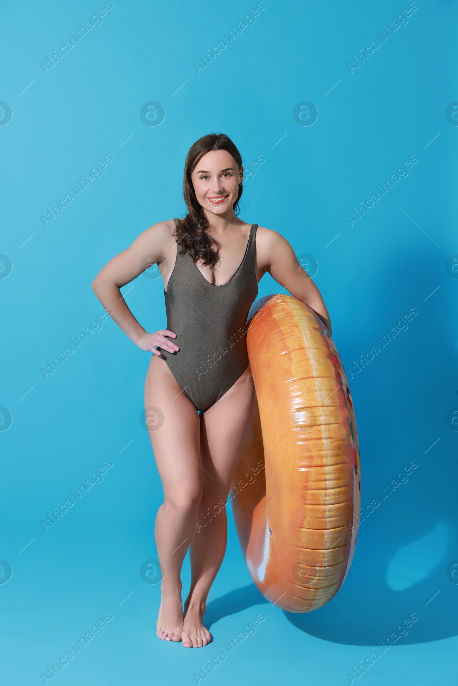 Photo of Beautiful woman in swimsuit with inflatable ring on light blue background