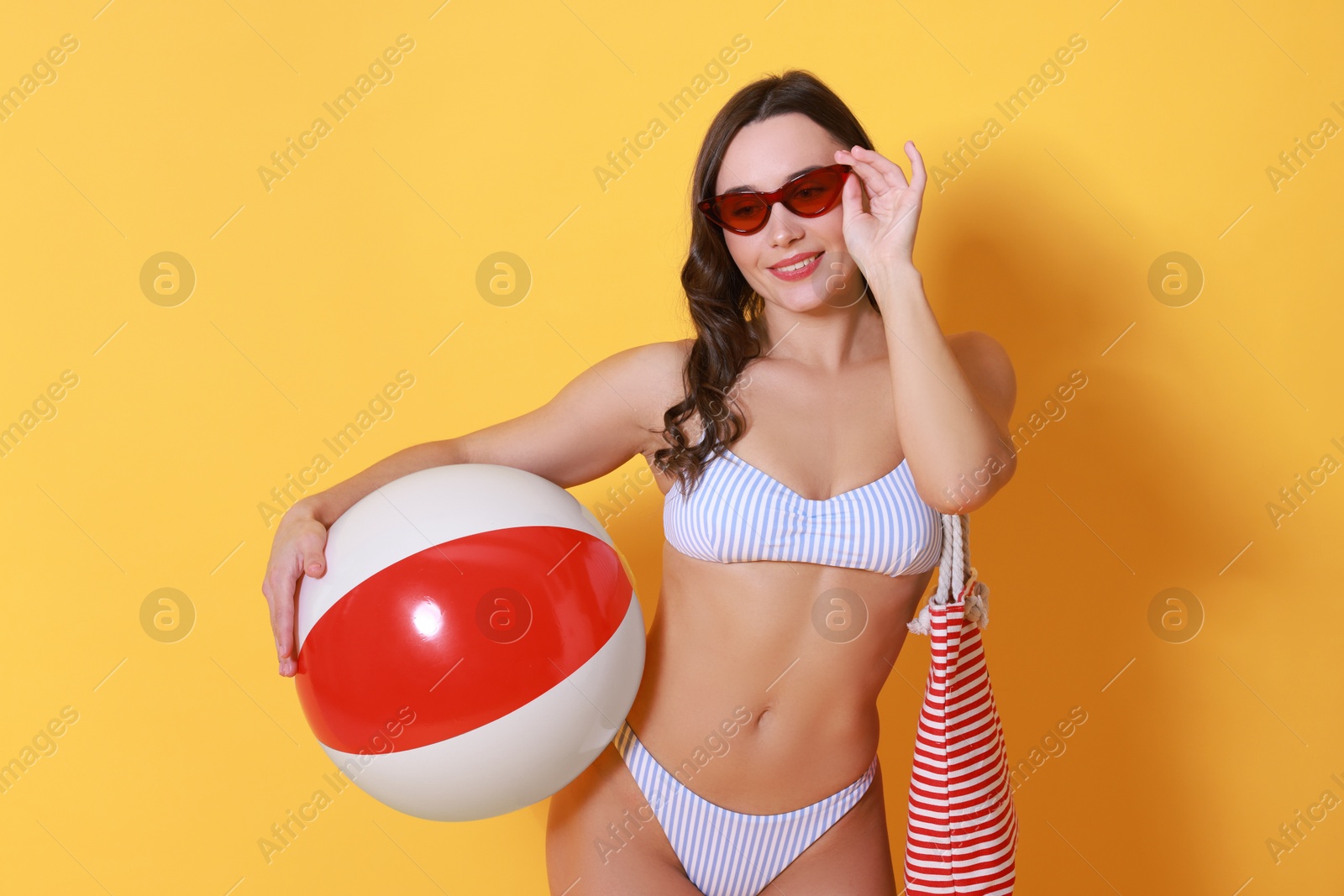 Photo of Beautiful woman in swimsuit with inflatable ball on yellow background