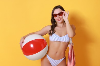 Photo of Beautiful woman in swimsuit with inflatable ball on yellow background