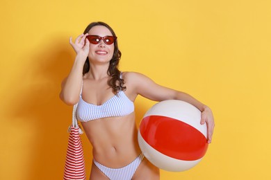 Photo of Beautiful woman in swimsuit with inflatable ball on yellow background