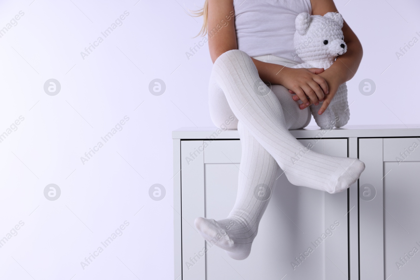 Photo of Child in tights sitting on cabinet against white background, closeup. Space for text