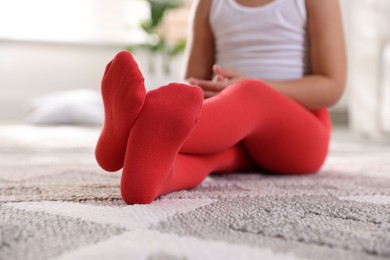 Photo of Child in red tights sitting on floor at home, closeup