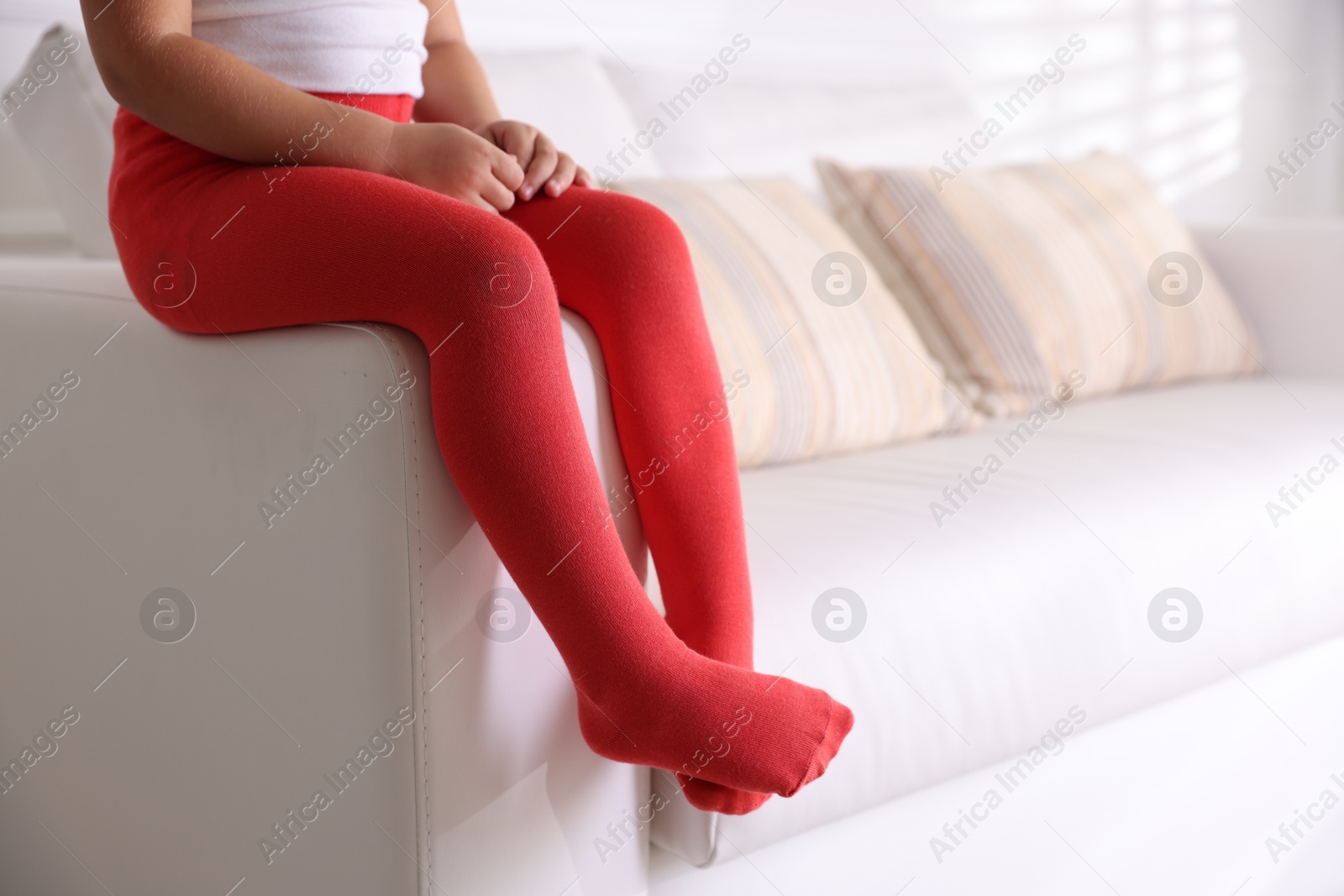 Photo of Child in red tights sitting on sofa at home, closeup. Space for text