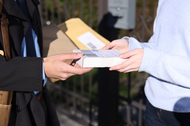 Photo of Postman giving parcel to woman outdoors, closeup