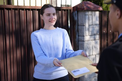 Photo of Young woman receiving envelope from postman outdoors, selective focus