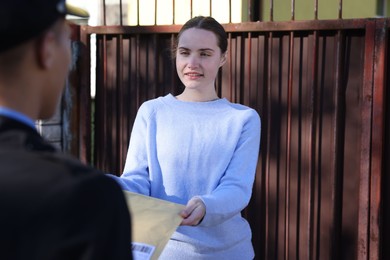 Photo of Young woman receiving envelope from postman outdoors, selective focus