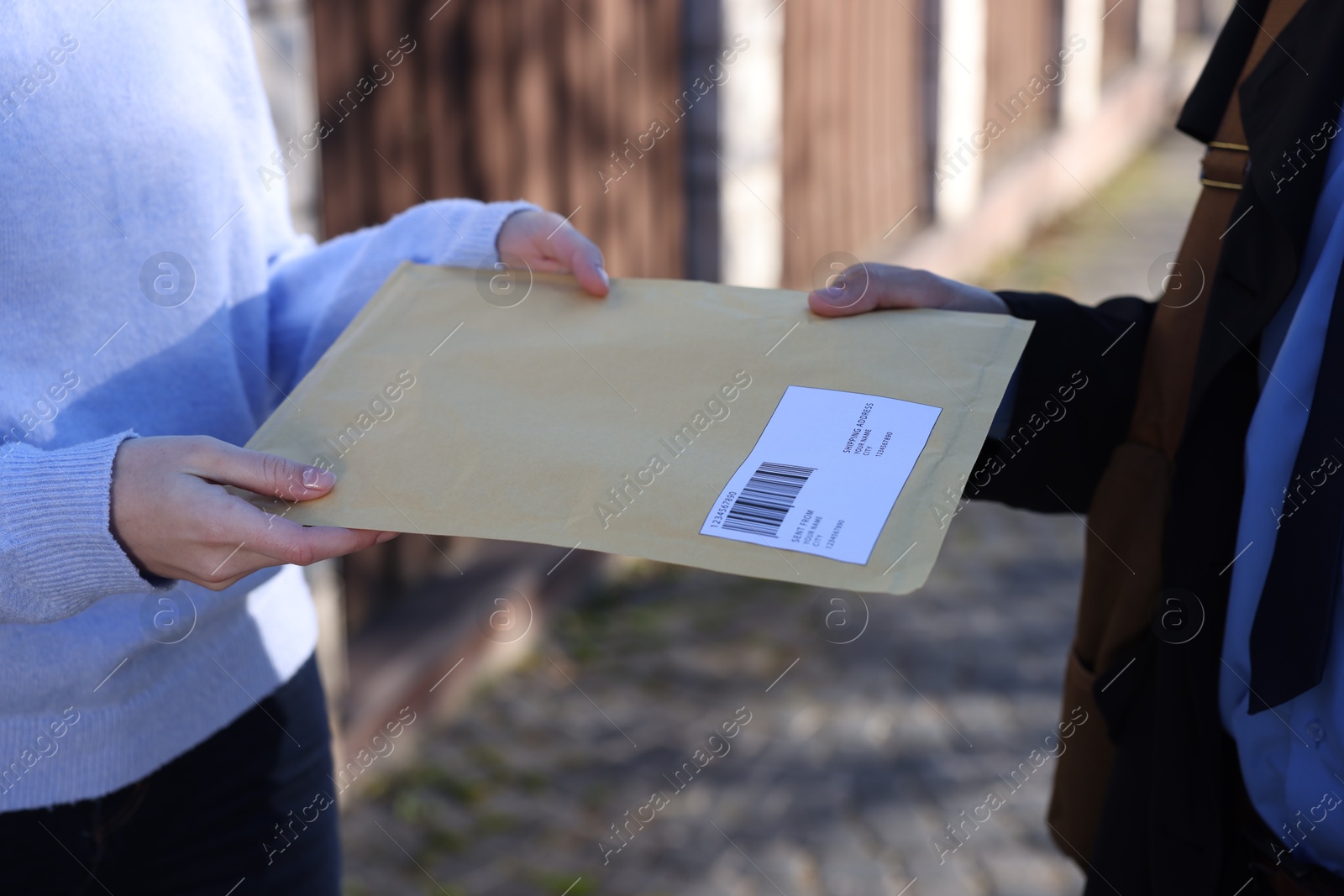 Photo of Postman giving envelope to woman outdoors, closeup