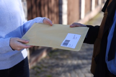 Photo of Postman giving envelope to woman outdoors, closeup