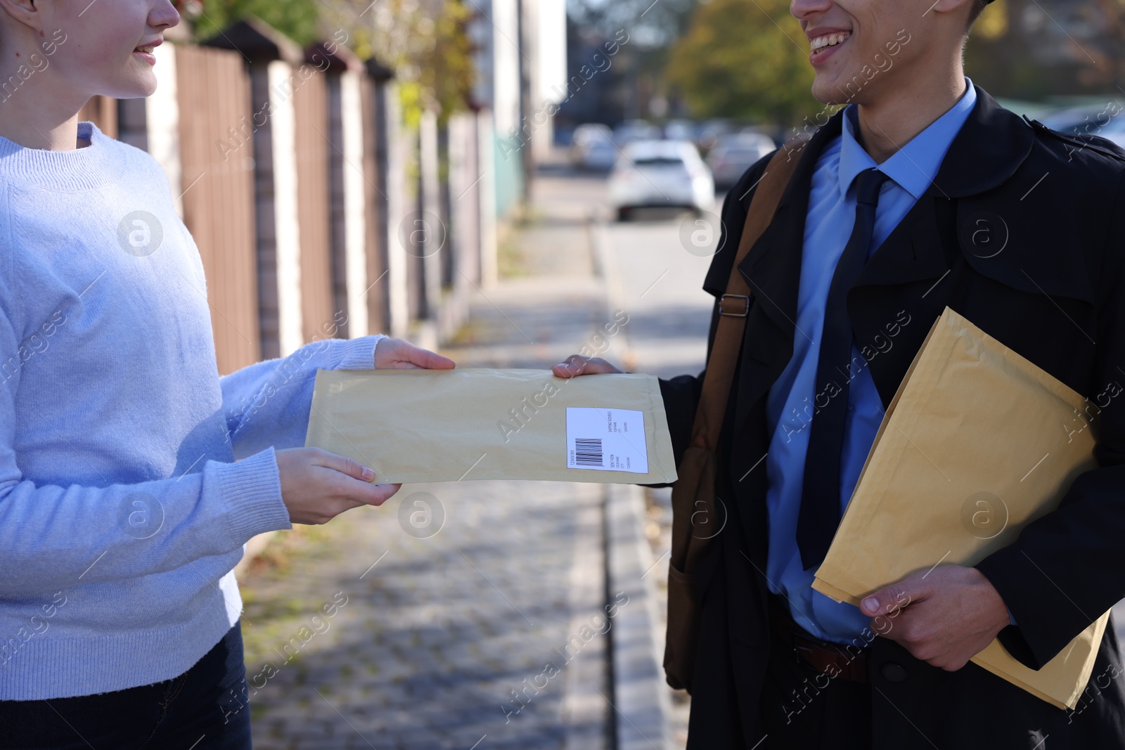 Photo of Postman giving envelope to woman outdoors, closeup