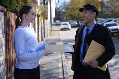 Photo of Postman giving envelope to young woman outdoors