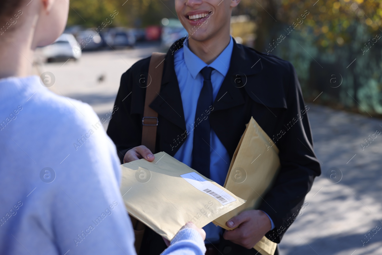 Photo of Postman giving envelope to woman outdoors, closeup