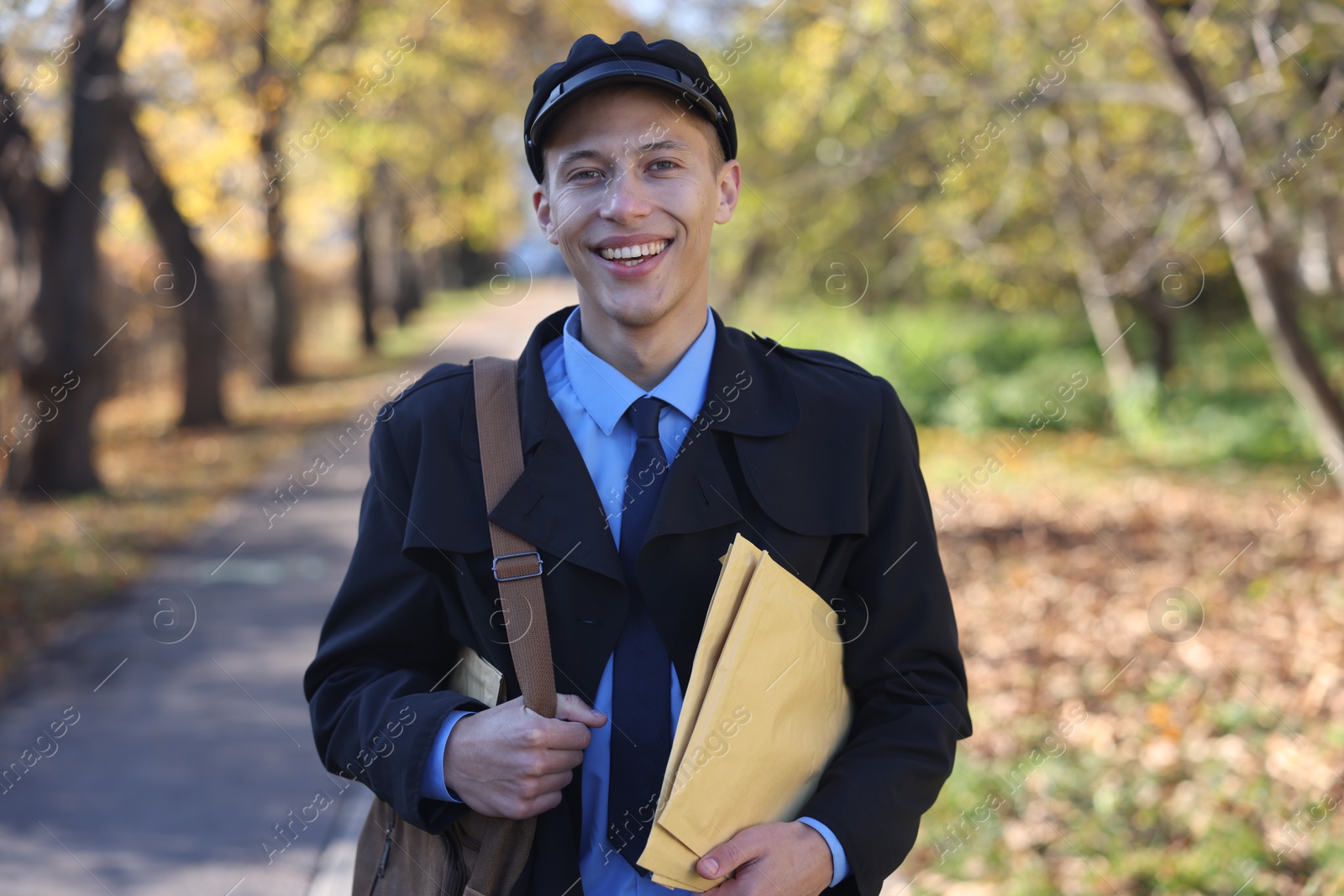 Photo of Happy postman with bag and envelopes outdoors