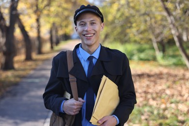 Happy postman with bag and envelopes outdoors