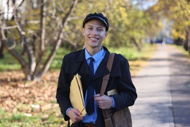 Happy postman with bag and envelopes outdoors