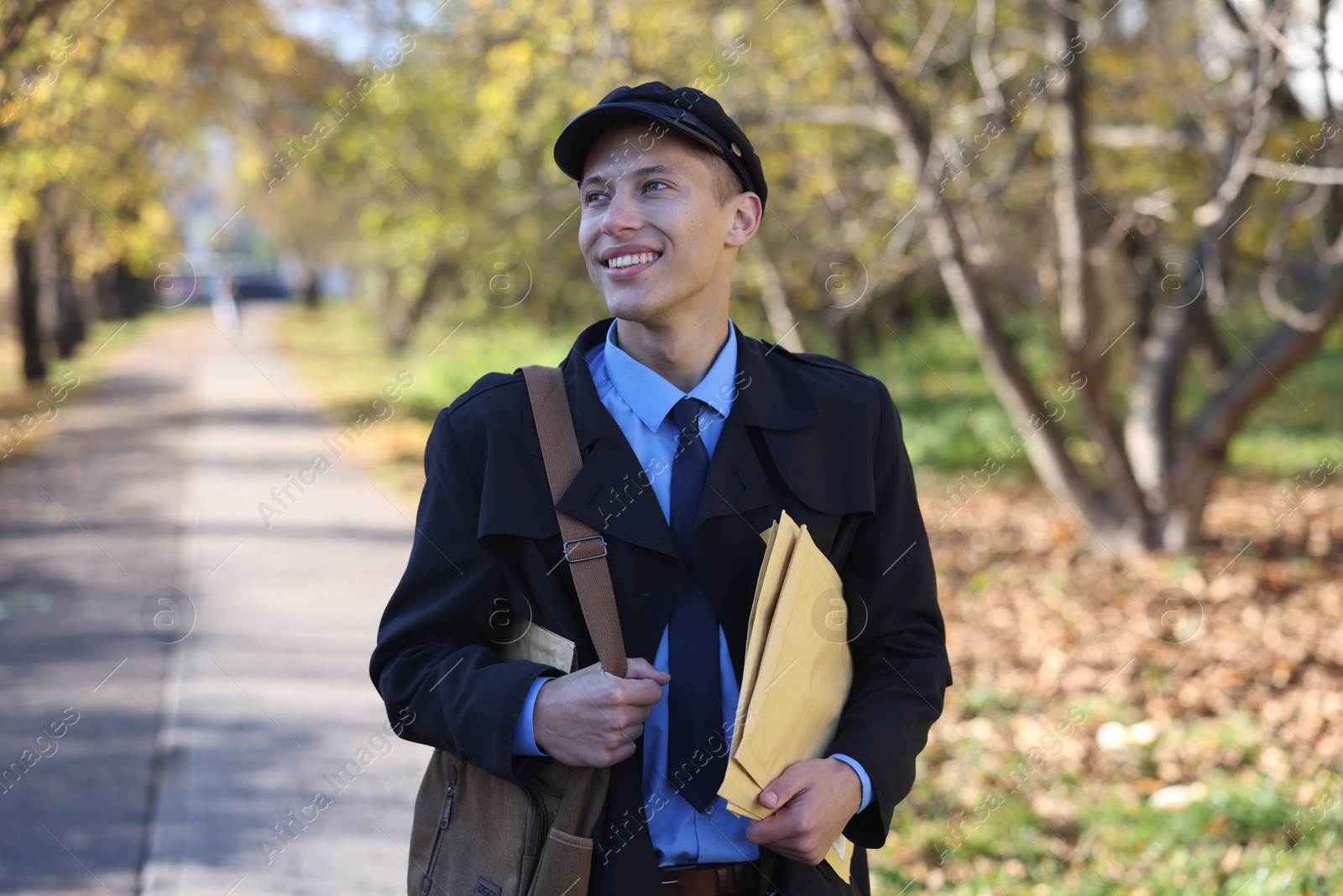 Photo of Happy postman with bag and envelopes outdoors