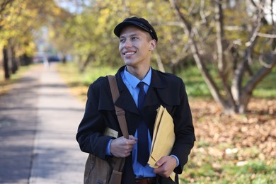 Happy postman with bag and envelopes outdoors