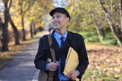 Happy postman with bag and envelopes outdoors