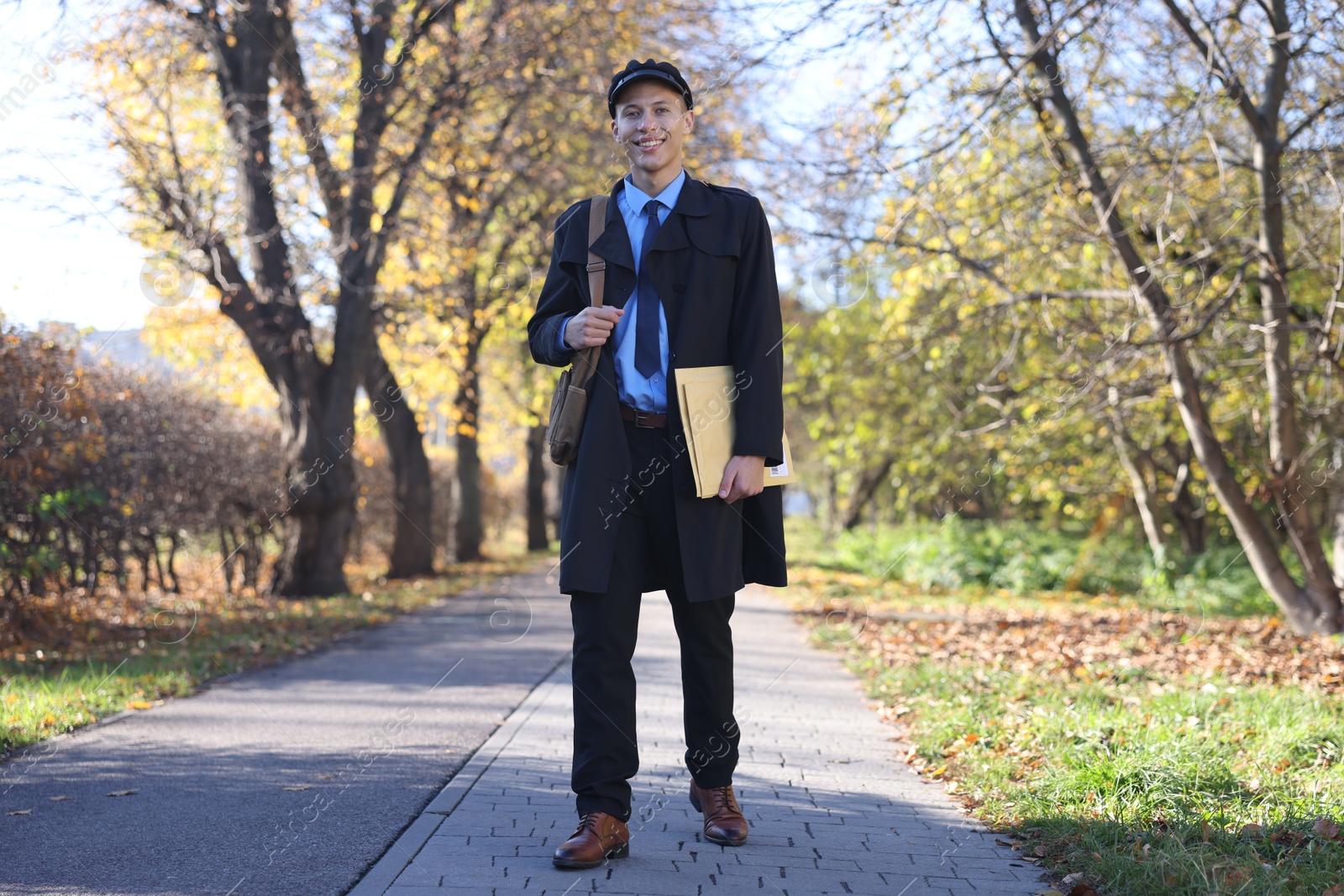 Photo of Happy postman with bag and envelopes outdoors