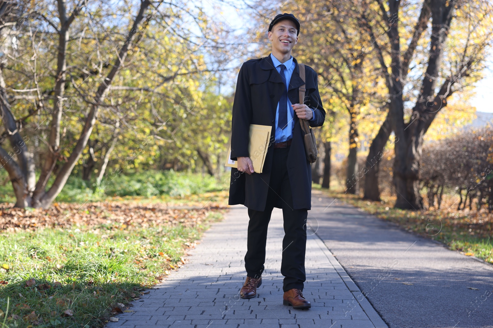 Photo of Happy postman with bag and envelopes outdoors