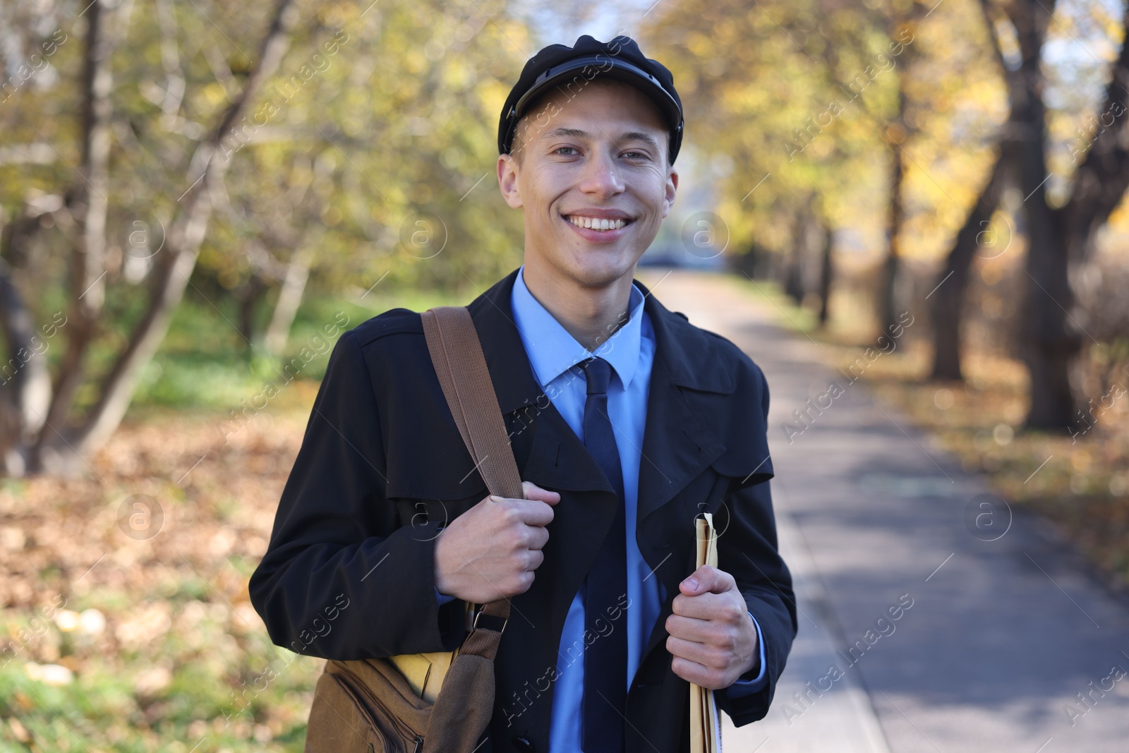 Photo of Happy postman with bag and envelopes outdoors