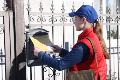 Photo of Postwoman putting envelope into mail box outdoors