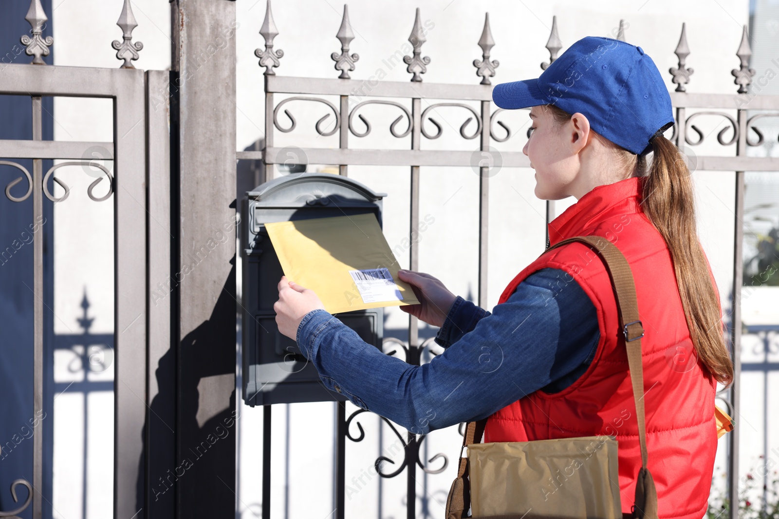 Photo of Postwoman putting envelope into mail box outdoors