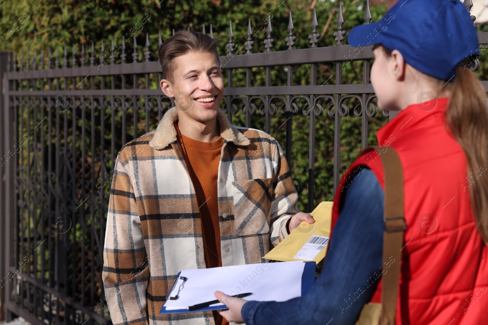 Photo of Young man receiving envelope from postwoman outdoors