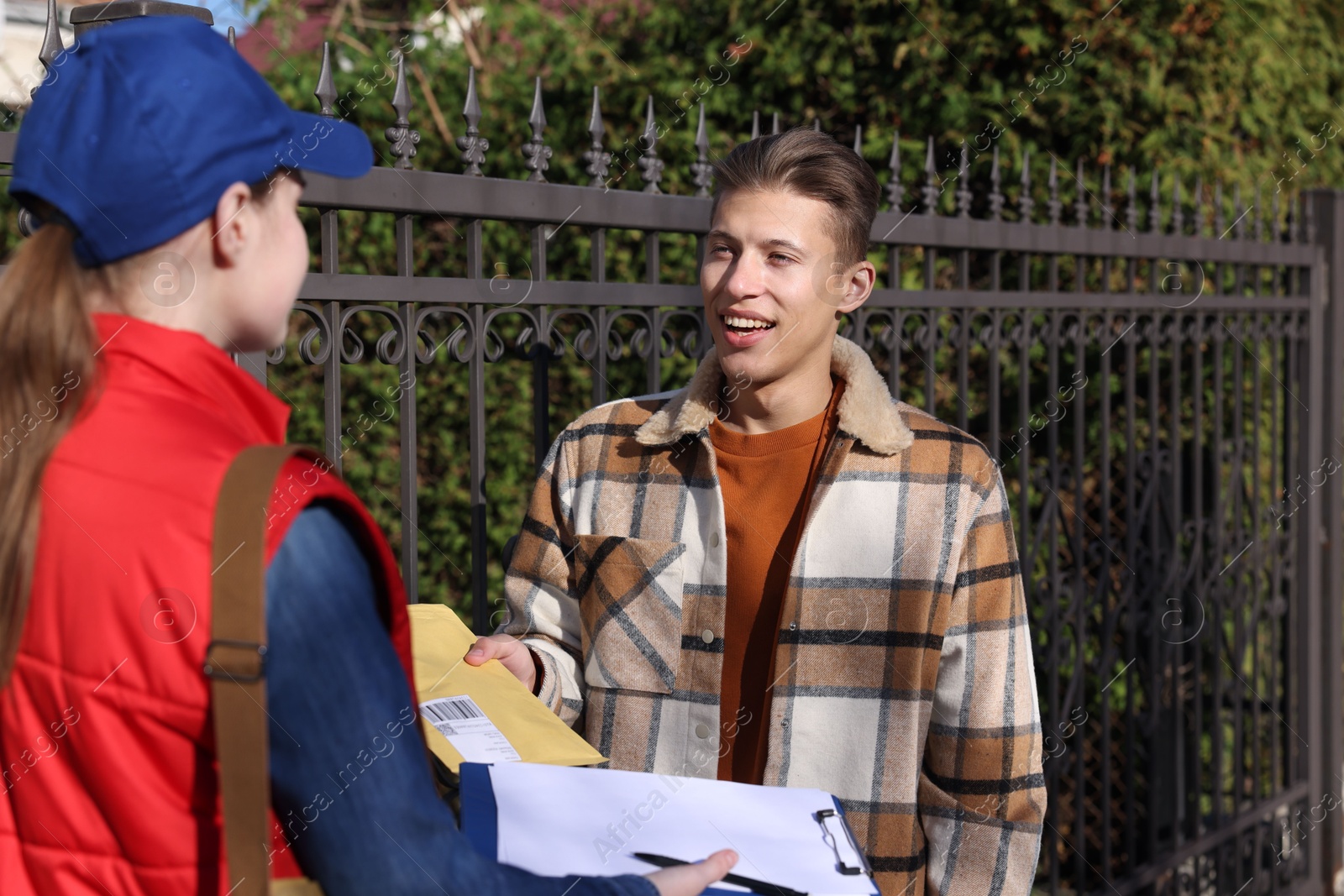 Photo of Young man receiving envelope from postwoman outdoors